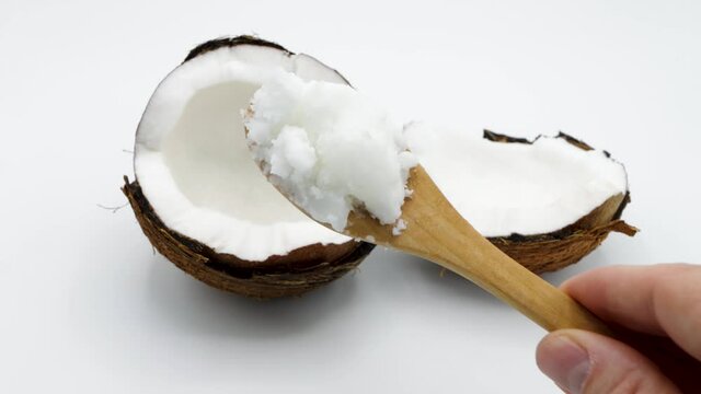 Showing a tablespoon of solidified coconut oil with a few coconuts on a white background