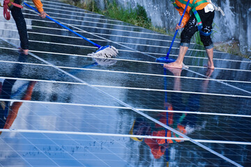 Technician is using a mop and water to clean the solar panels that are dirty with dust and birds' droppings to improve the efficiency of solar energy storage even better. Soft and selective focus.