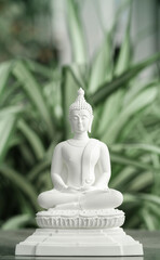 White Buddha statue meditating among nature background.