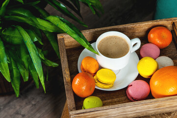 French colored macaroons with white cup of coffee on wooden background