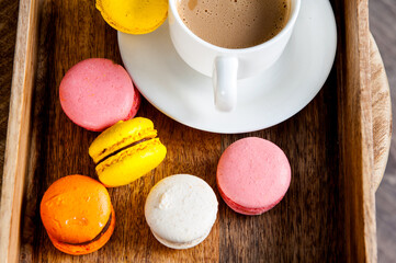 French colored macaroons with white cup of coffee on wooden background