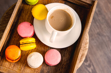 French colored macaroons with white cup of coffee on wooden background