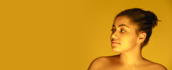 Naklejka premium Flyer. Beautiful african-american woman's portrait isolated on yellow golden studio background in neon, monochrome. Concept of human emotions, facial expression, sales, ad, fashion and beauty.
