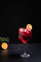 Cóctel rojo en vidrio decorado con rodaja de naranja sobre fondo negro