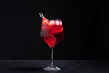 Cóctel rojo en copa con una rodaja de naranja sobre fondo negro