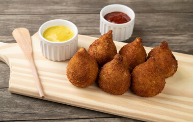 Typical brazilian snack coxinha on a wooden board with ketchup and mustard