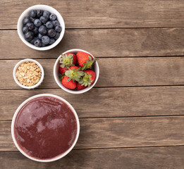 Brazilian typical acai bowl with fruits and muesli over wooden background with copy space