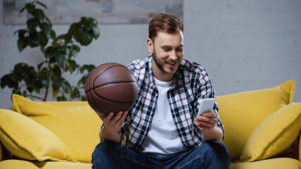 happy basketball fan holding ball and watching match on smartphone - Powered by Adobe