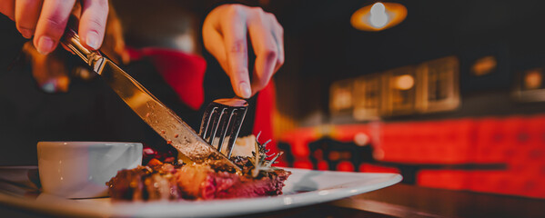 woman hands with fork and knife eating beef steak in cafe