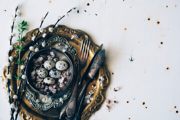 Vintage or rustic Easter table setting from above. Plate, cutlery, eggs on and natural spring branch on rustic wood. Country style. Copy space. Toned image.