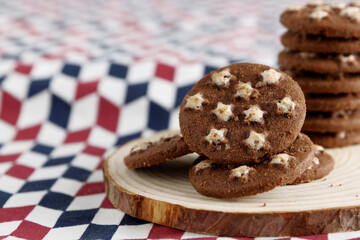 Heap of cocoa cookie biscuits with stars pattern on wood slice and checkered kitchen towel.