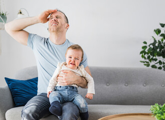 Man holding a screaming baby the father have headache