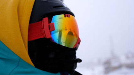 Fototapeta na wymiar Man in a helmet and glasses riding a mountain on a lift with a snowboard on a background of snowfall.