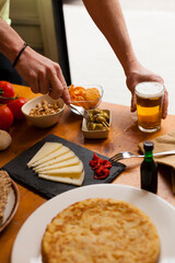 Vertical Spanish tapas bar table with various typical dishes and beer with hands acting.  