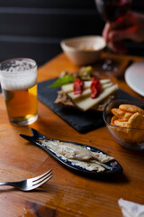 Vertical low key shot of bar food table with anchovies in vinegar and other tapas with beer and wine. Spanish food gathering concept.