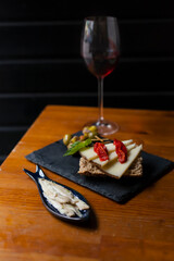 Spanish tapas concept with a plate of anchovies and a gourmet cheese and pepper on bread appetizers with glass of wine on second term on a wooden table on a black background. 