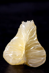 Piece of white pomelo fruit flesh on dark background. Fresh citrus fruit chunk.