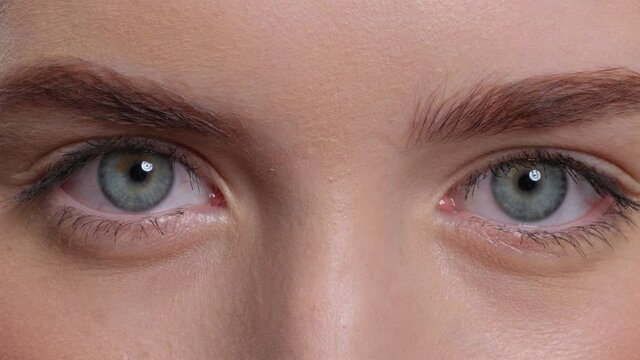 Close up on bright blue eyes of a beautiful young woman. Studio portrait of a beautiful model girl with perfect skin. Pretty girl with clean fresh skin. Beauty and skin care. Cosmetology. 4K footage. 