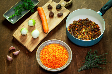 Cooking red lentil and dried apricot soup. Ingredients on wooden board, plates and pan.