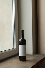 Blank white label mock up on black bottle of unlabeled red wine on a wooden windowsill. Alcohol...