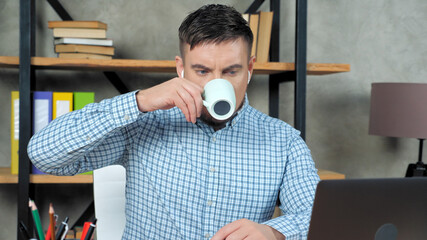 Focused businessman wear wireless earphones drinking coffee tea listen financial report company top manager employee remote online video call conference webcam meeting chat laptop computer in office