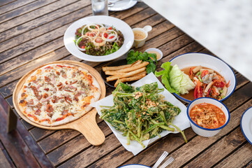 Variety of food with pizza meat cheese, crispy vegetable, spicy salad and crockery on wooden table