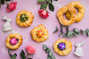 Homemade easter buns with colorful easter eggs on pink background, top view