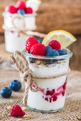 Yogurt with berries and cereals in a glass on a rustic wooden table, vertical