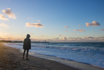 adolescent seul face à la mer et devant le soleil couchant  et le phare des Baleines sur l'île de...