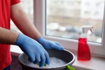 A young guy in a red T-shirt holds a sponge in his hands and is going to wet it in water for cleaning windows. Window cleaner concept