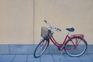 Fototapeta na wymiar A red bicycle with a basket stands against the background of a beige wall.