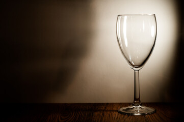 An empty glass stands on a wooden shelf. Light falls on it.