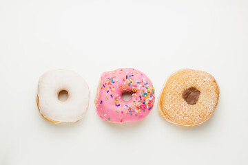 Overhead flat lay view of three fresh, colourful ring doughnuts in a row isolated on a plain white...