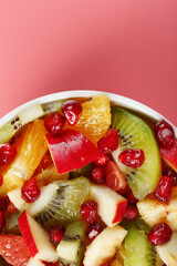 Bowl with fruit salad on a pink background. Juicy and ripe fruit slices.