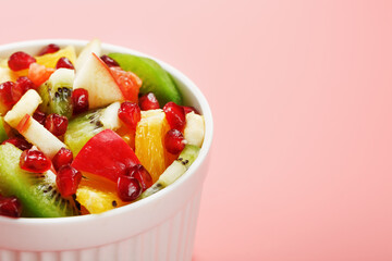 Bowl with fruit salad on a pink background. Juicy and ripe fruit slices.