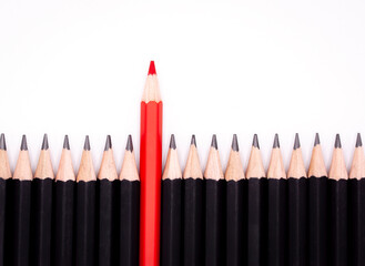 Red pencil in the middle role of black pencil out from crowd of plenty identical black fellows to show leadership, independence, strategy, think different concept.
