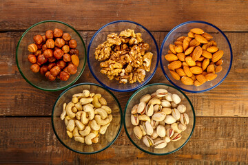 Assorted nuts in a glass bowl on a wooden table.