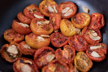 Grilled tomatoes topping with garlic on the black plate.