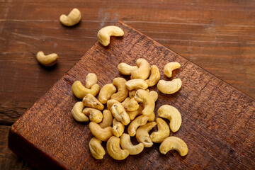 Cashew nuts scattered on a square board on a wooden table.