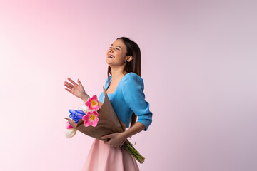 The cheerful girl, good mood, smiles positively, dressed in fashion clothes, bouquet of tulips, meeting with her friend, receives the proposal to get married isolated on neon pink. 