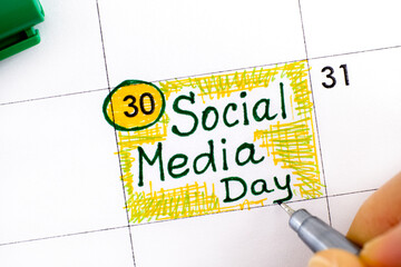 Woman fingers with pen writing reminder Social Media Day in calendar.