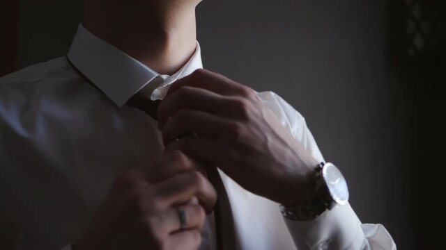 A businessman man in a white shirt tightens his tie around his neck.