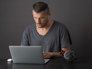 Man wearing wireless earphones, editing video from camera on laptop.