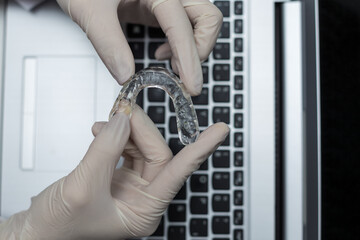 Dentist examining a transparent silicone orthodontic with his hands and noting the quality of the material on the computer.