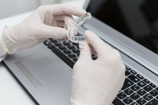 Dentist examining a transparent silicone orthodontic with his hands and noting the quality of the material on the computer.