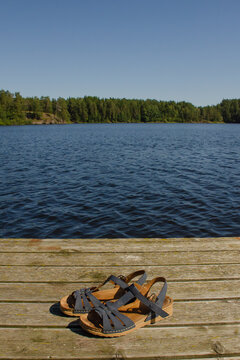 Blue women's sandals on a wooden pier in summer against the background of water and sky. Travel hiking concept, vertical photo