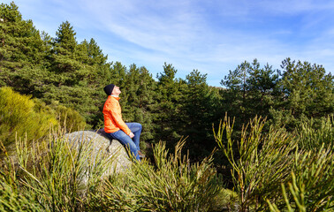 Man with his face to the sun in the mountains, sitting on a rock, on a cold spring morning.