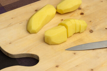 Peeled potatoes and knife on wooden board