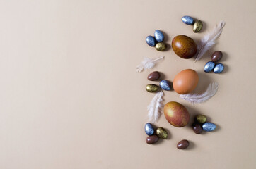 Festive Easter minimalist background. Natural brown eggs lie on a beige background, candy jelly, almonds in chocolate of different colors lie nearby. Copying space, flat layout