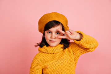Funny kid posing with peace sign. Studio shot of caucasian preteen girl in yellow outfit.